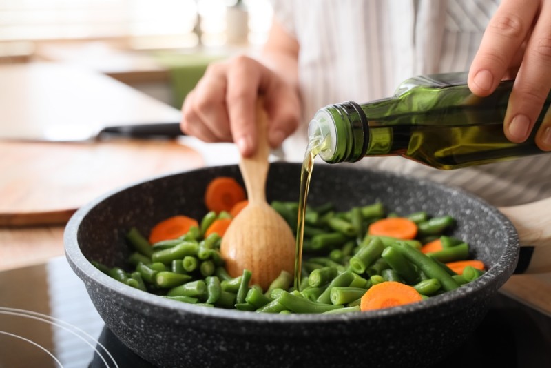 persoana toarna ulei intr-o tigaie cu legume
